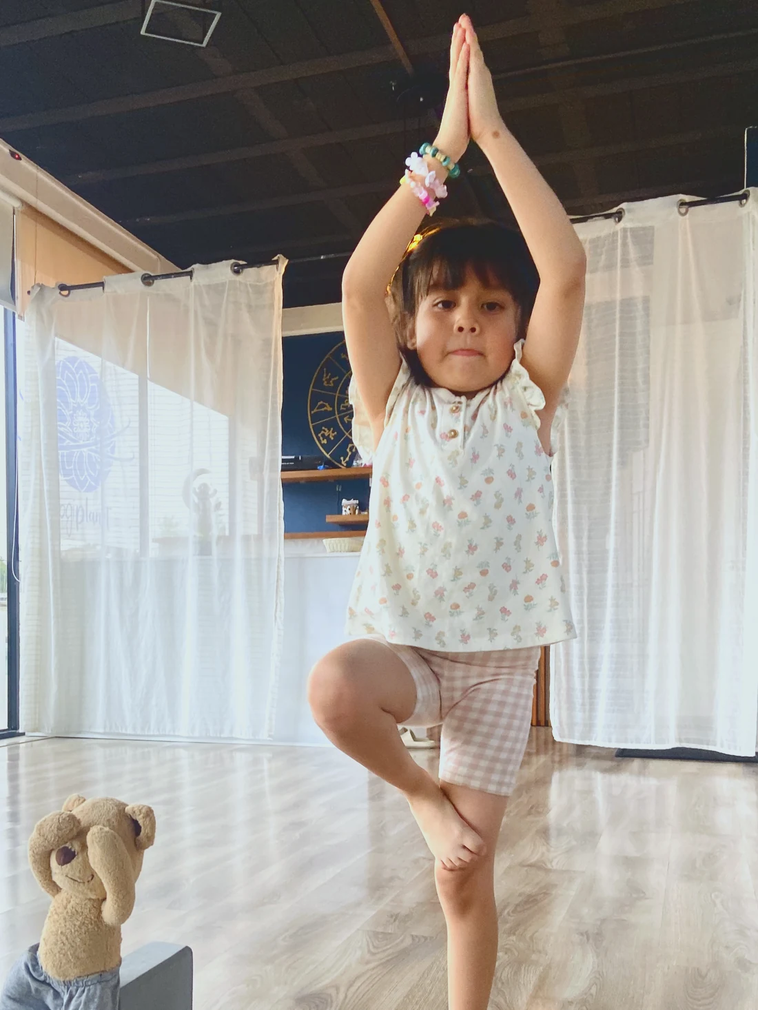 Una niña en clase de yoga en el estudio, meditando con su oso de peluche