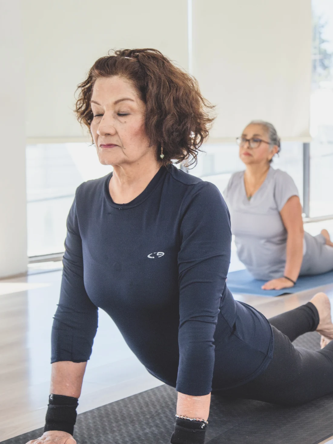 Una alumna mayor en clase de yoga suave, con la instructora acompañándola